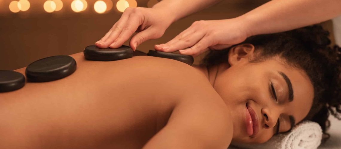 Healing hot stone massage for joyful black woman at luxury spa, closeup